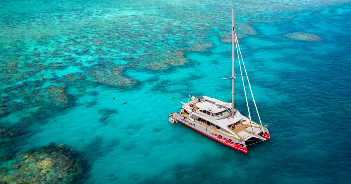 Passions of Paradise sailing catamaran moored over shallow outer reef patches off Cairns, turquoise water and coral bommies around it