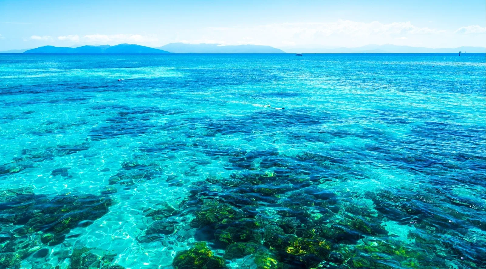 Clear turquoise water over a shallow coral reef flat with a coastline on the horizon