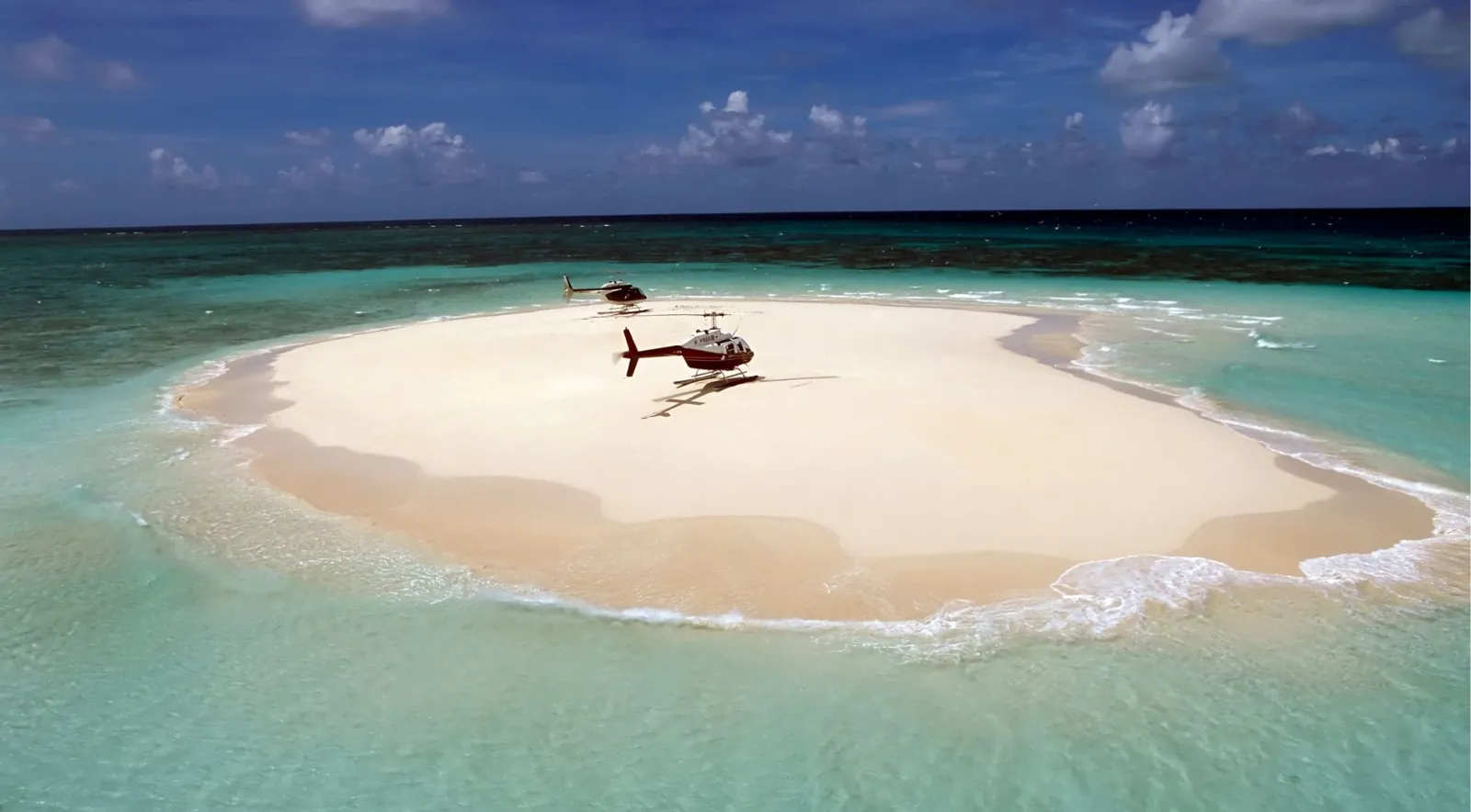 Helicopter parked on a white sand cay surrounded by shallow reef water