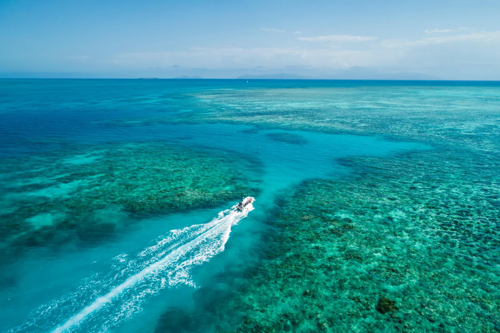 Aerial view of a boat wake across a shallow reef lagoon