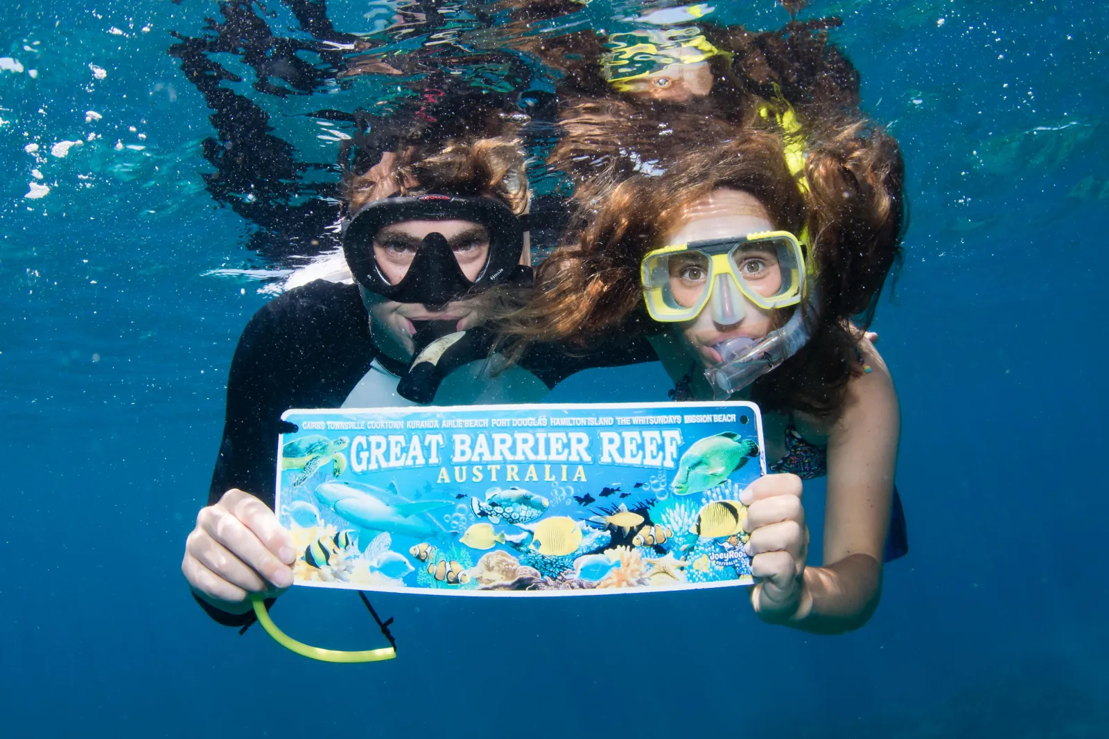 Two snorkellers holding a Great Barrier Reef sign underwater