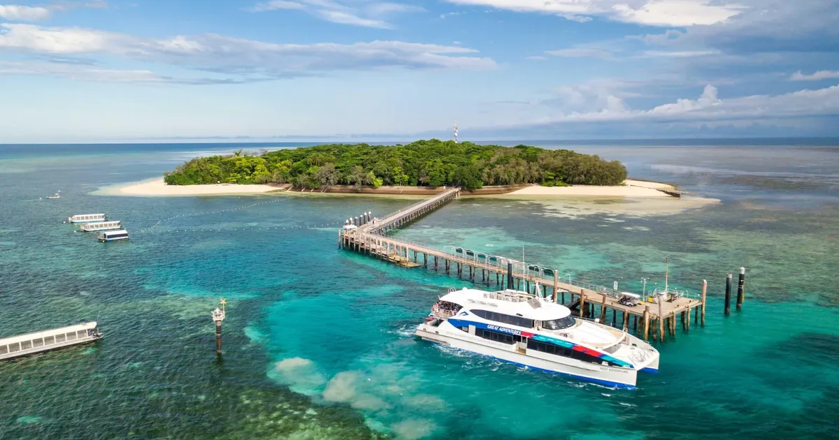 Aerial view of Green Island off Cairns, a rainforest-covered coral cay with a white beach and a long jetty where a reef catamaran is berthed